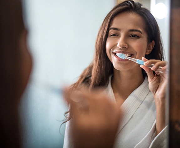 Woman smiling while brushing her teeth and looking in mirror