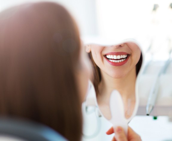 Woman with porcelain veneers looking at her smile in the mirror