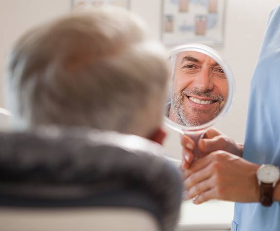 Man looking at smile in mirror after dental crown placement