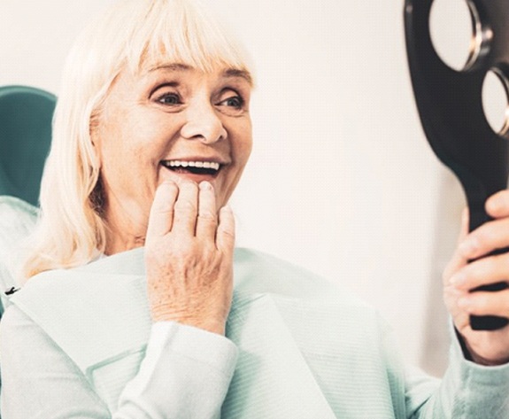 Smiling woman admiring her new dentures in Greensboro