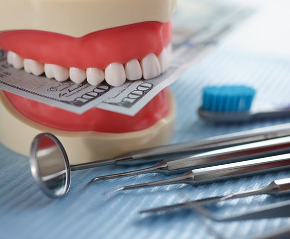 A model jaw biting dollar bills set next to dental tools