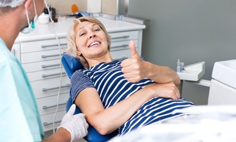 Woman smiling in dental chair with thumb up
