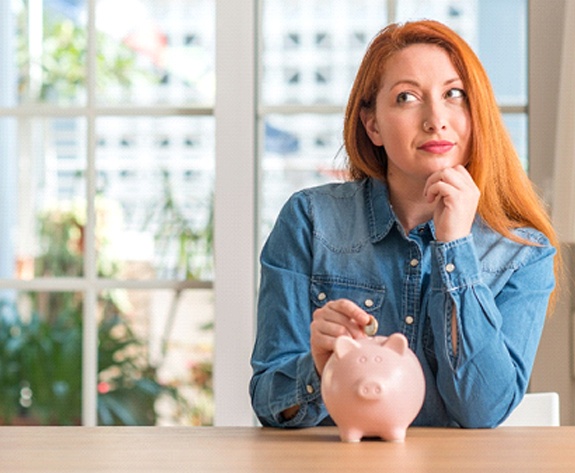 Woman putting coin in piggy bank for Invisalign in Greensboro