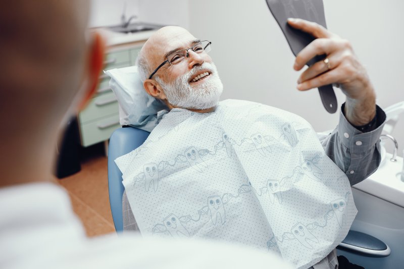 An old man admiring his smile in a hand mirror