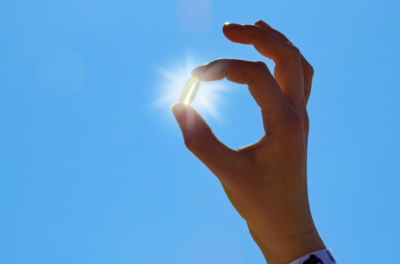 Close up of person holding a vitamin D pill up to the sun.